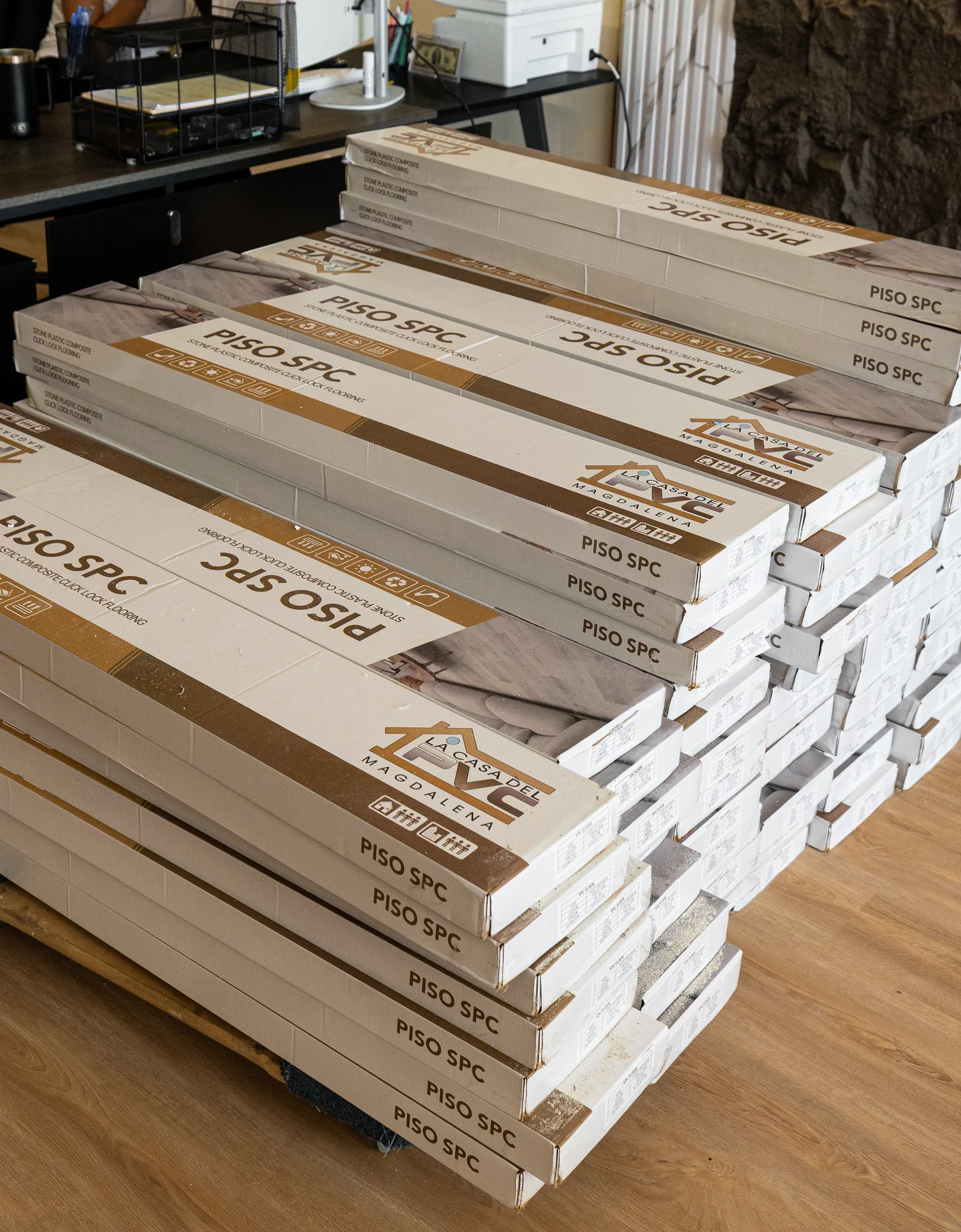 Stacks of piso spc flooring boxes on a light brown wooden floor in a store. by PVC Global Imports USA LLC in Bayonne, NJ